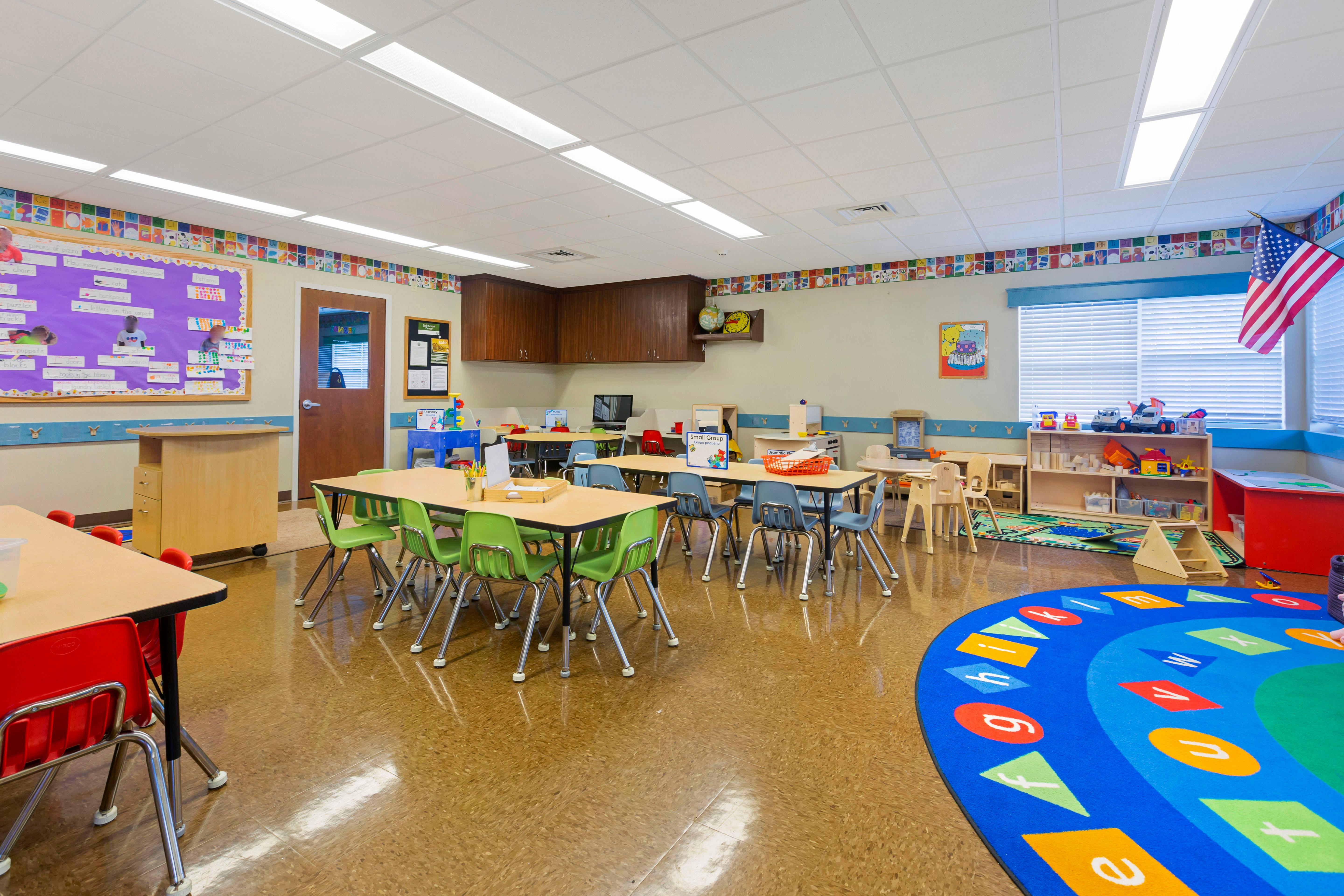 Classroom with child-sized tables and chairs, a play area, and an American flag
