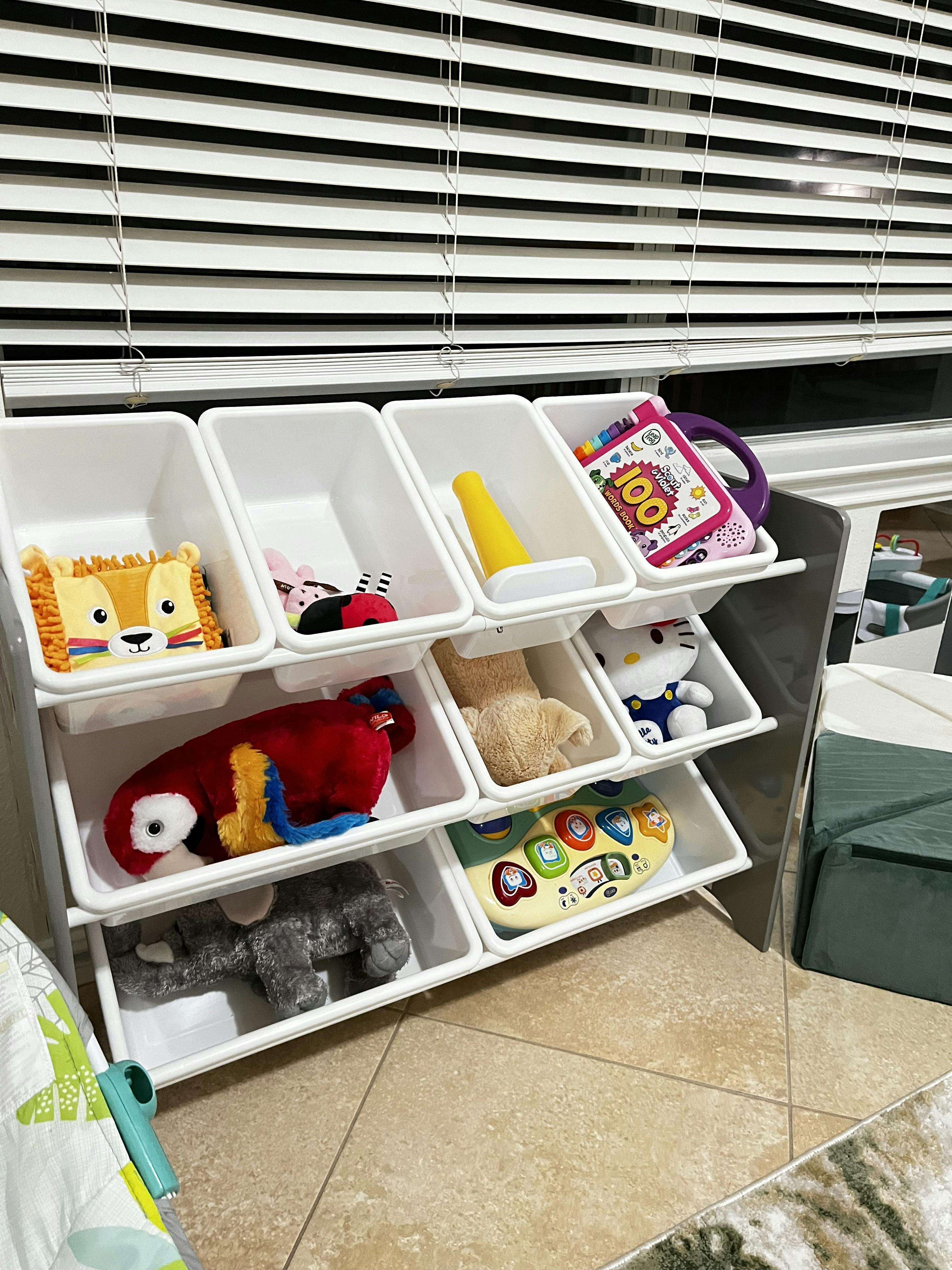 Toy organizer with white bins filled with plush animals and baby toys