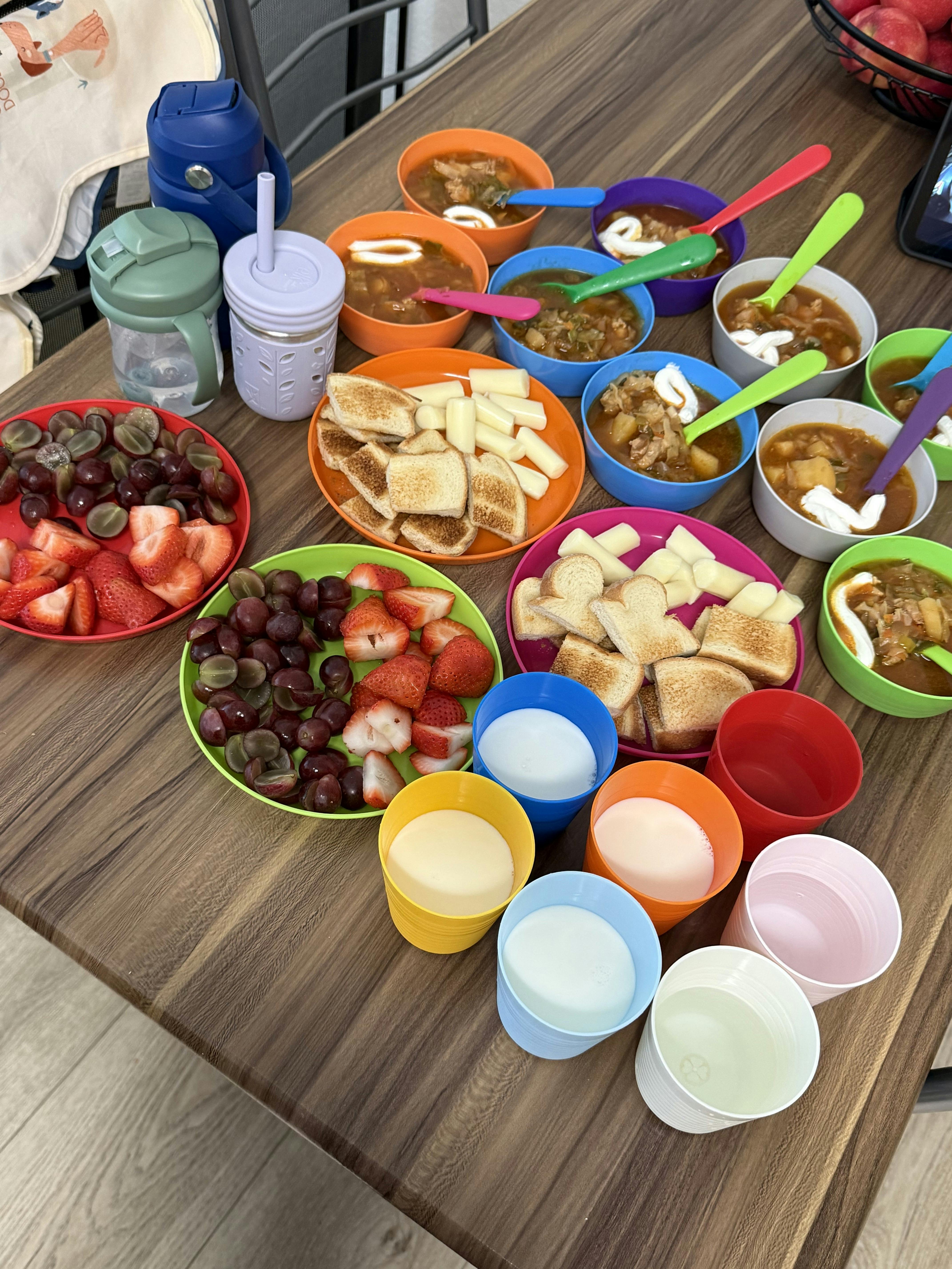 bowls of soup, fruit plates with toast, and colorful cups on a table