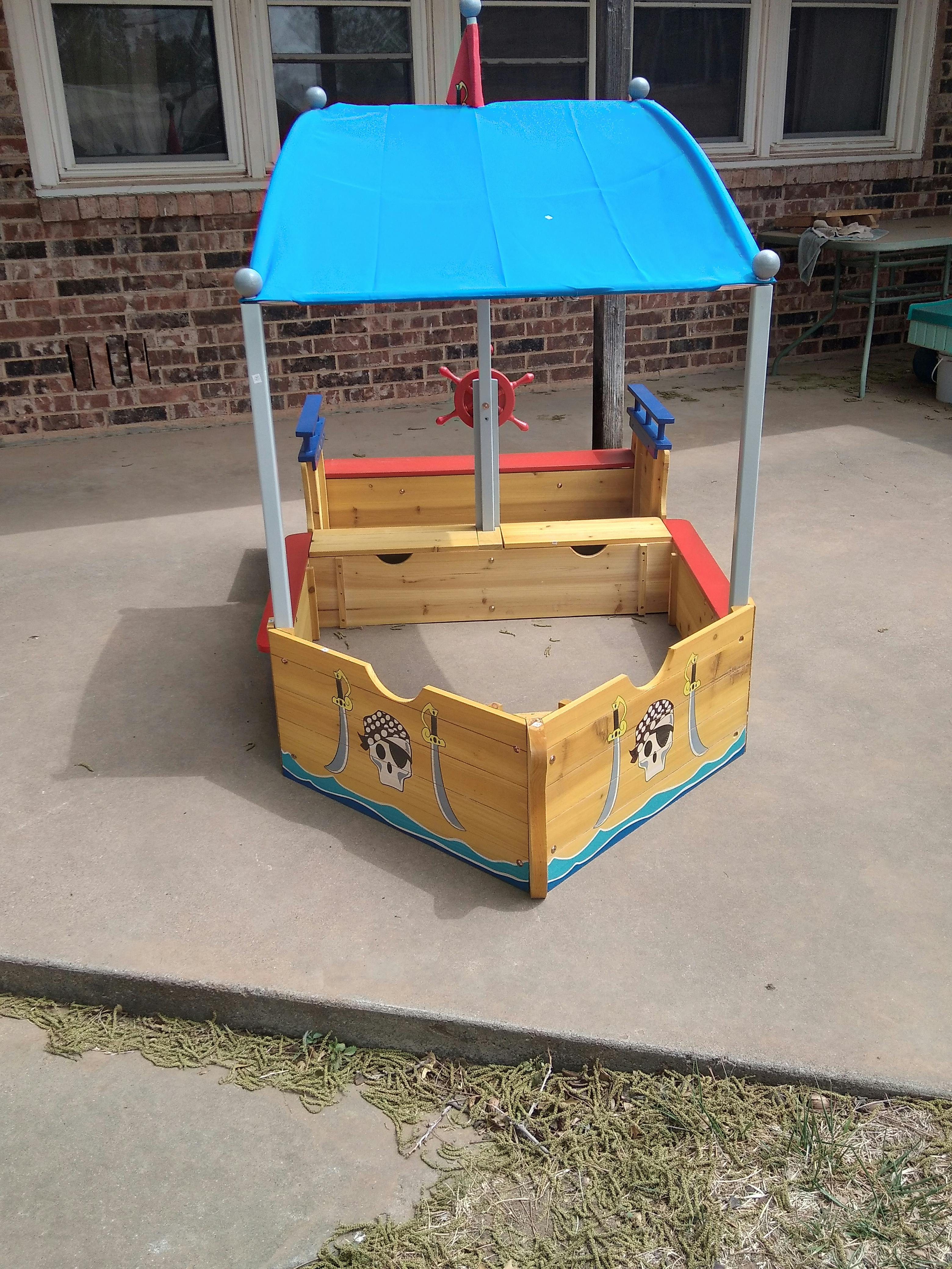 Wooden sandbox shaped like a pirate ship with a blue canopy