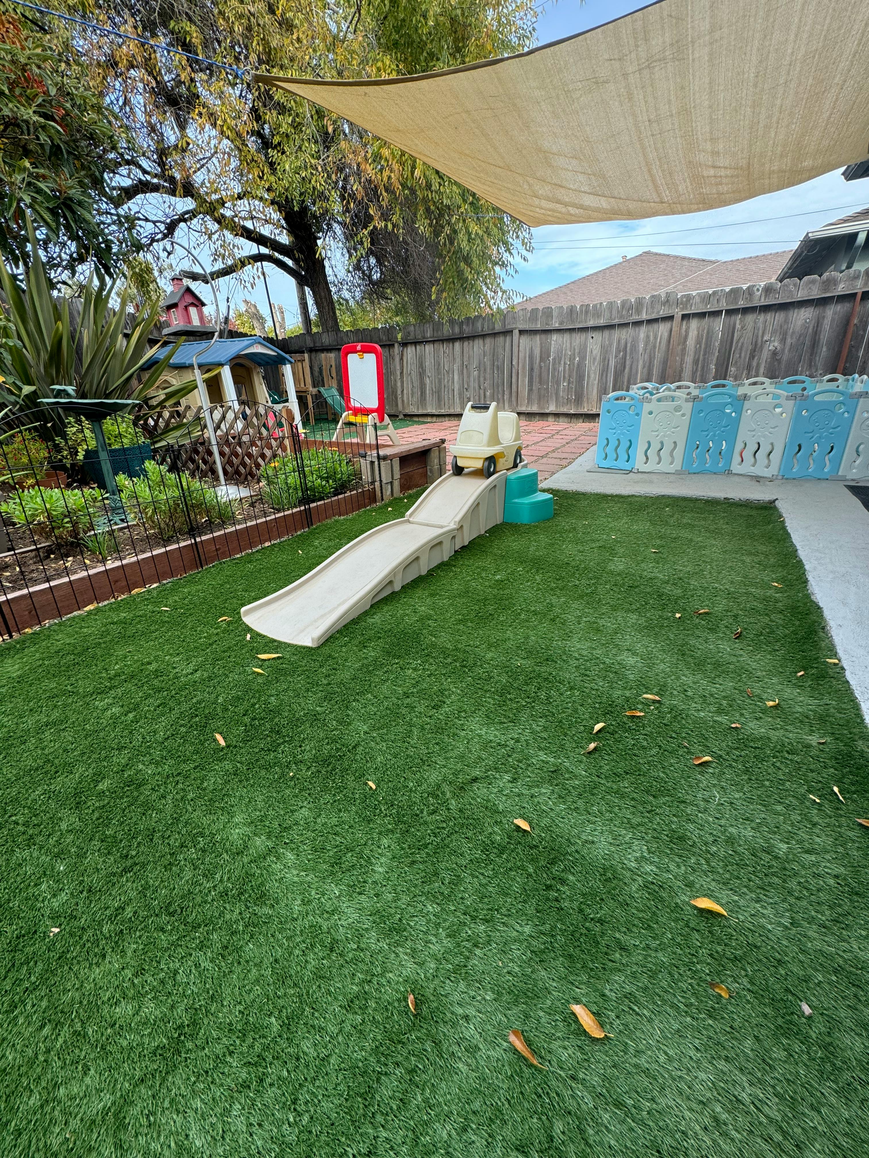Backyard with artificial turf, a small slide, and play structures