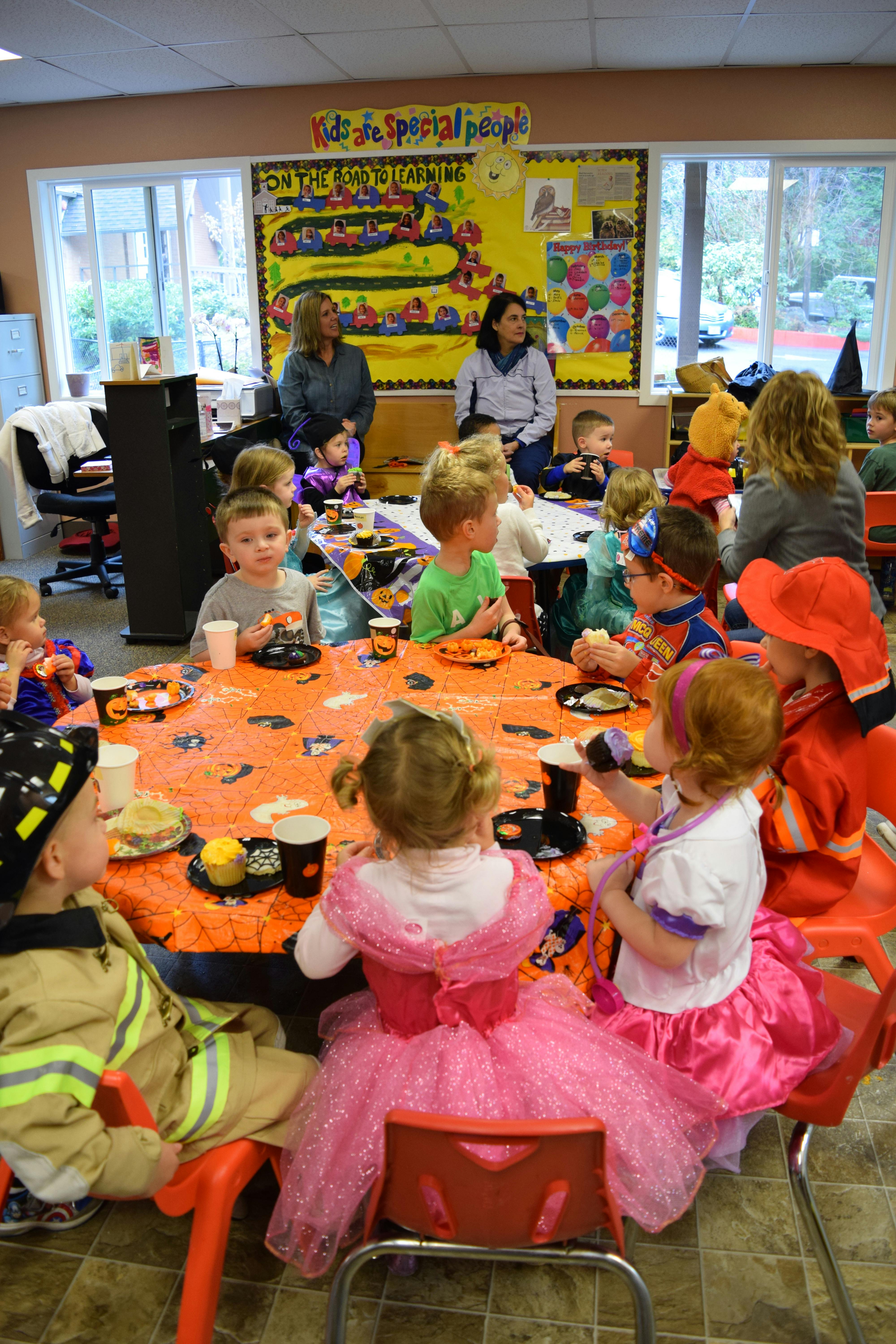 Children and adults gathered around tables in a classroom