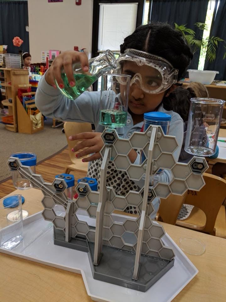 Child in safety goggles pouring liquid into a science experiment setup