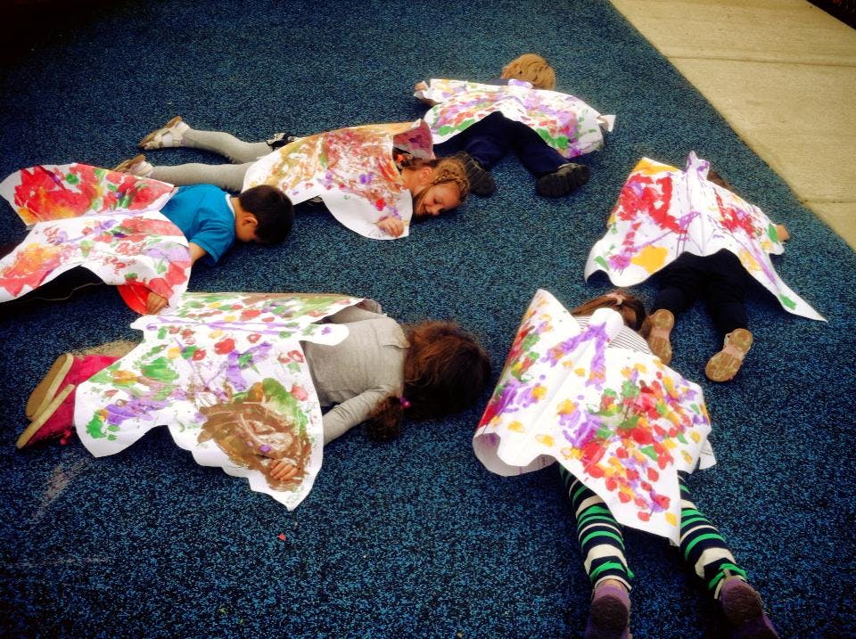 Children lying on the floor with paper cutouts on their backs