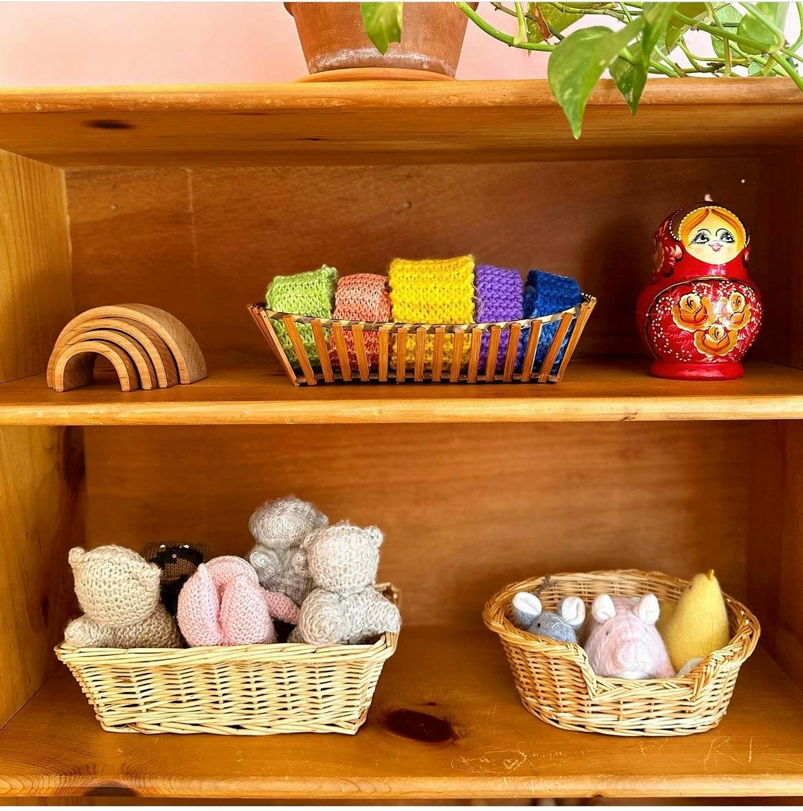 Wooden shelves with baskets of toys, including knitted bears and a nesting doll