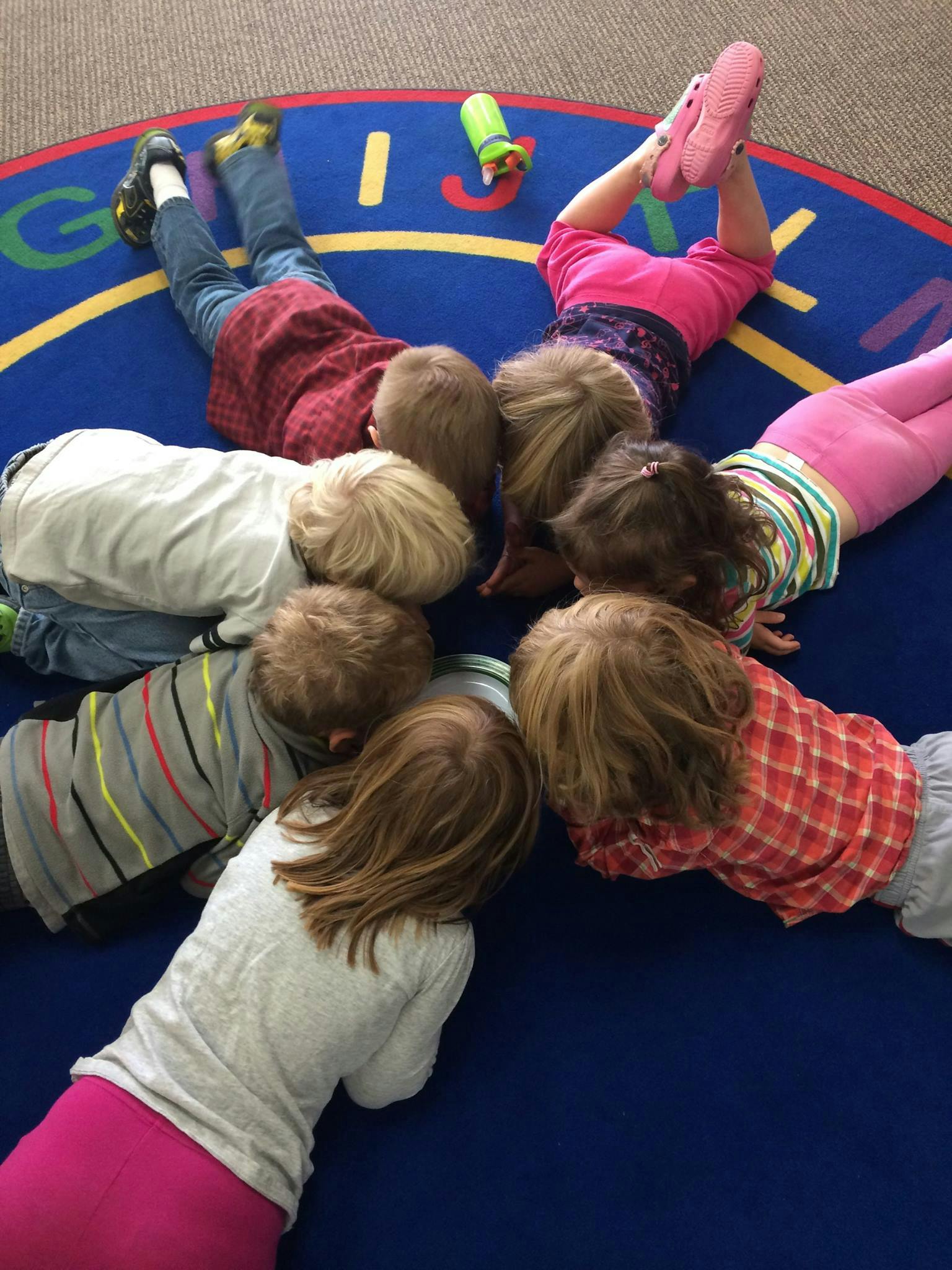 Children lying on a blue alphabet rug in a circle