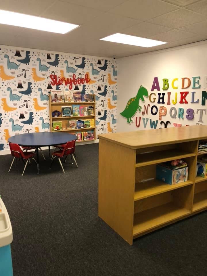 Children's classroom with dinosaur wallpaper, a bookshelf, and a table with chairs