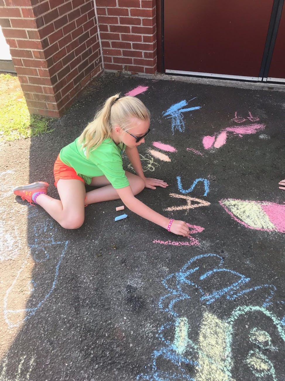 Child kneeling on pavement drawing with chalk