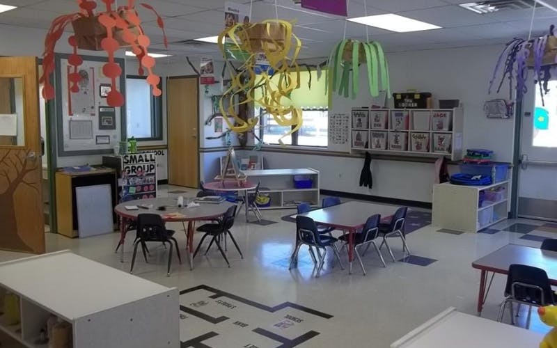 An empty elementary school classroom with small tables and chairs