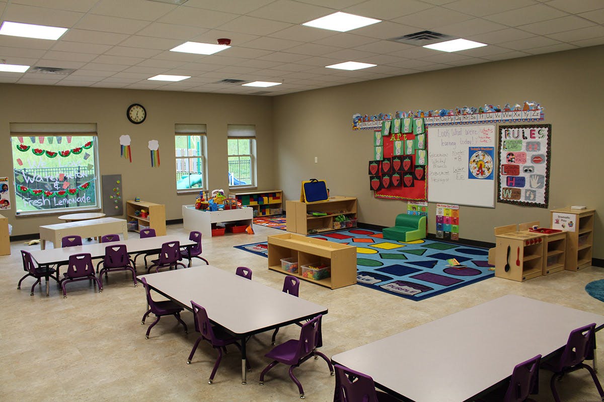 Empty classroom with small tables and chairs, colorful rug, and learning materials