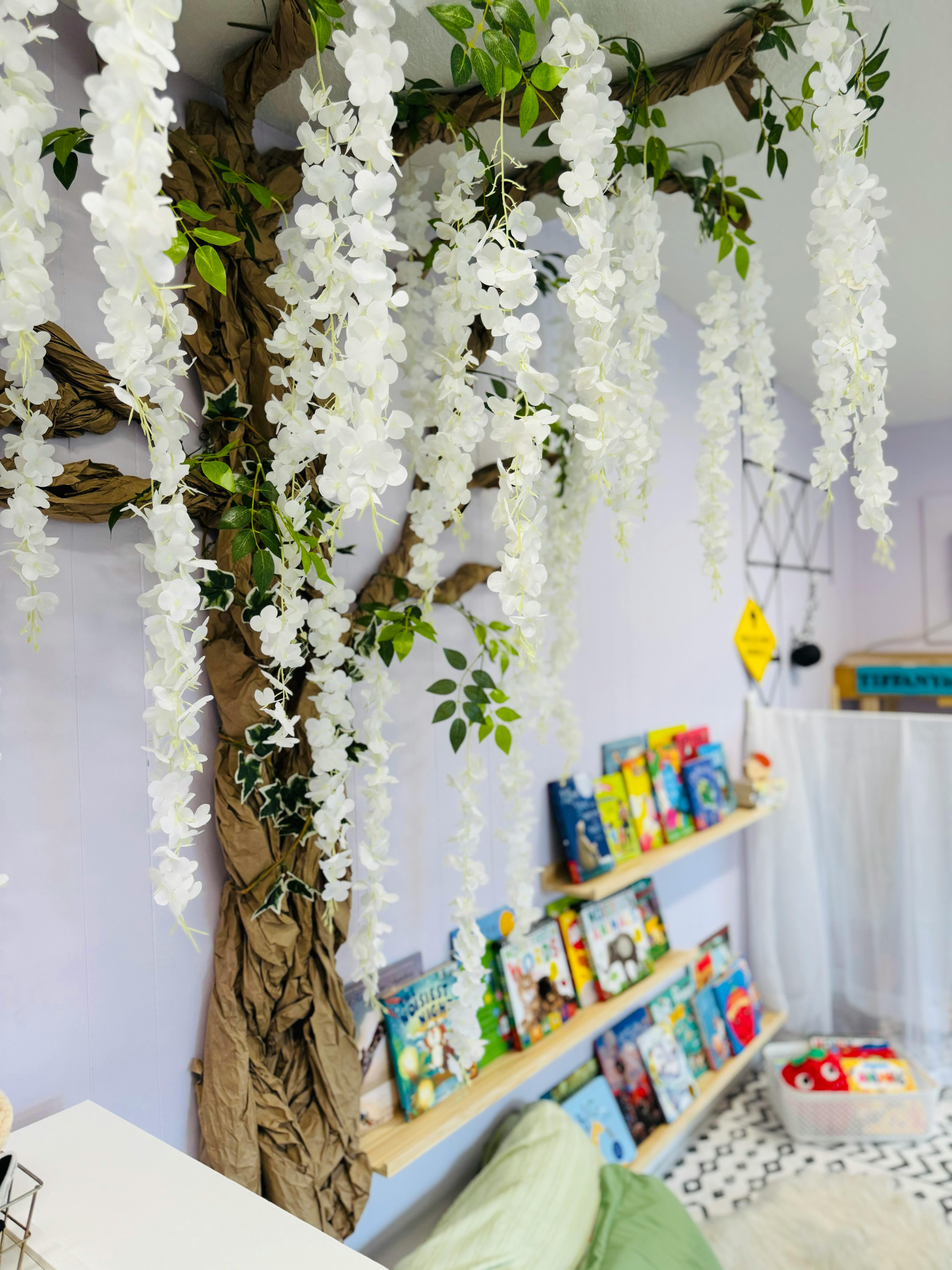 Decorative tree with white flowers and books on shelves in a room