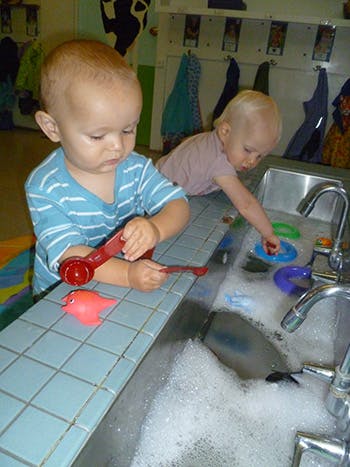 Two children playing with toys in a sink full of bubbles