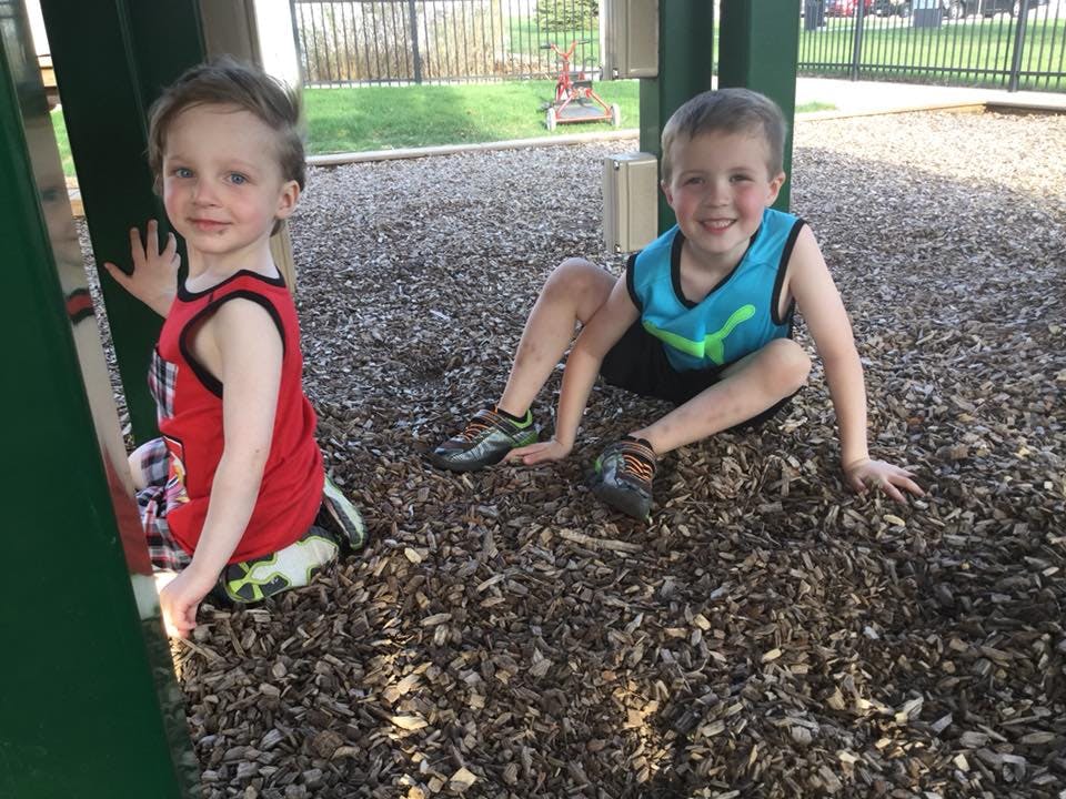 Two children sitting on wood chips in a playground