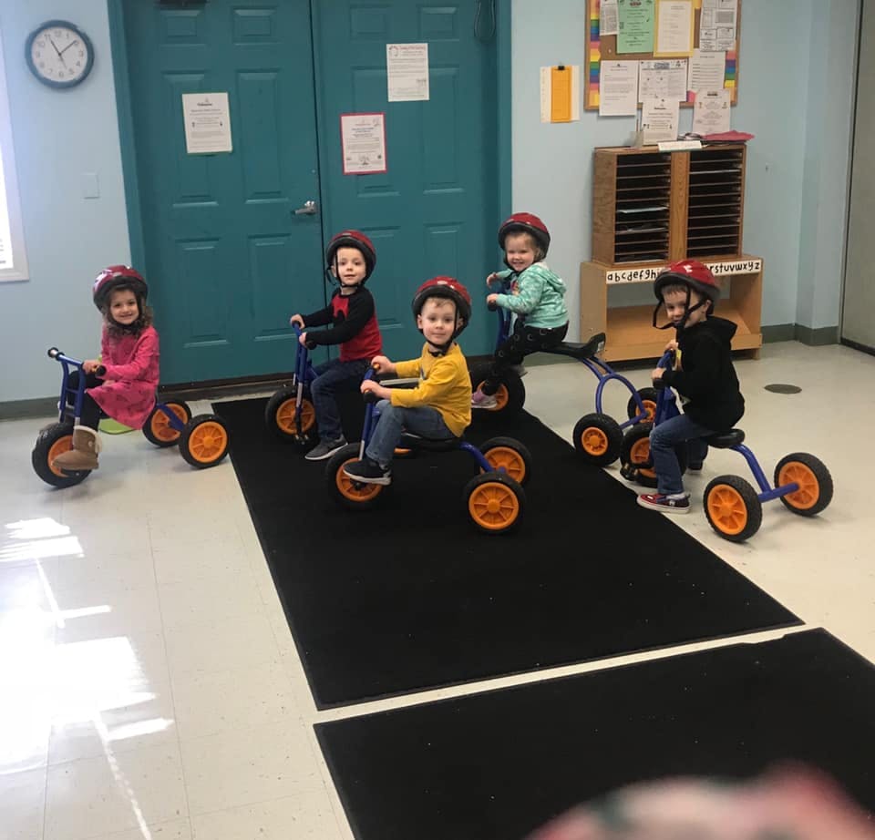 Children wearing helmets riding tricycles indoors