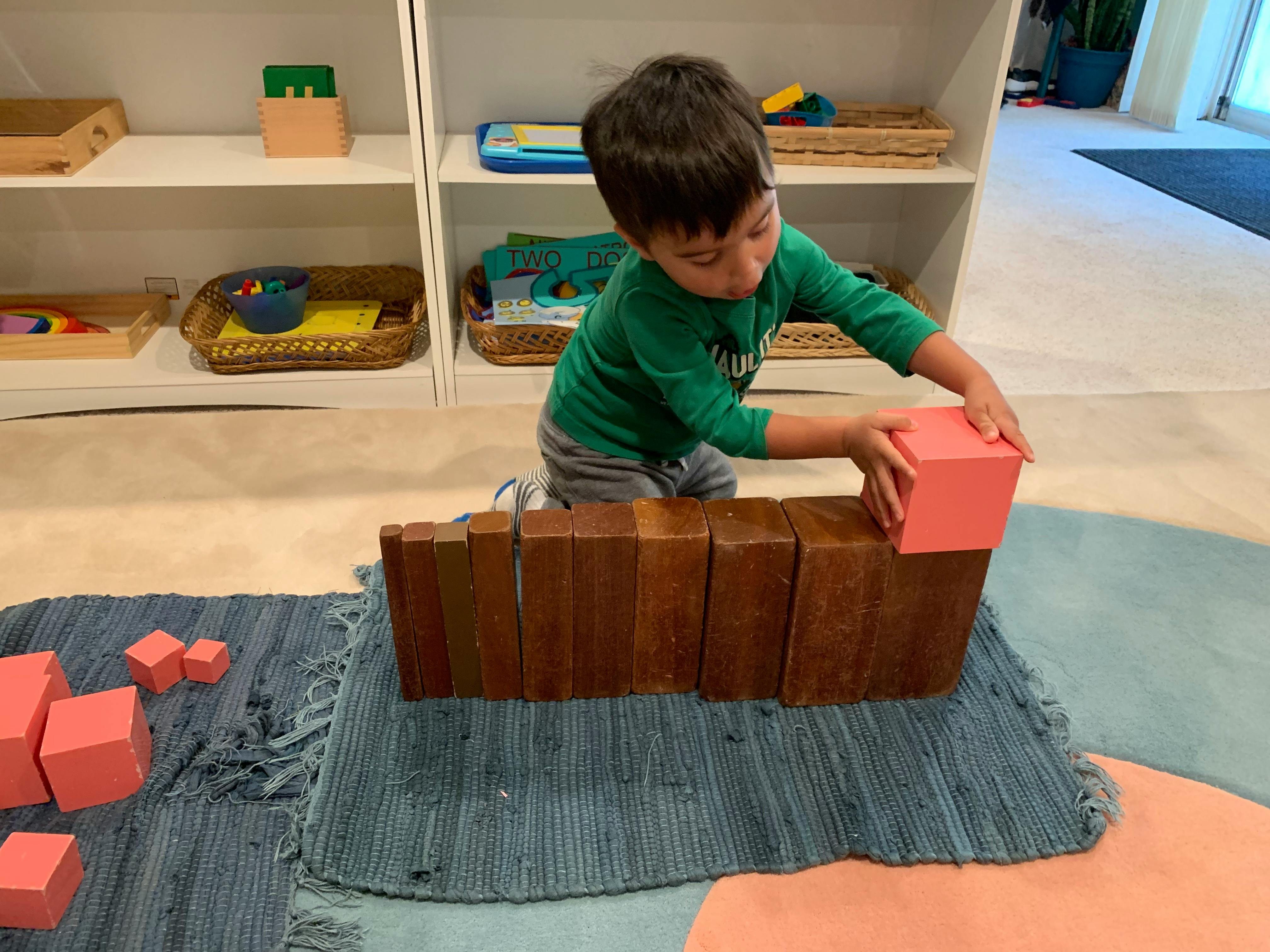 Child placing a pink block on a wooden block structure