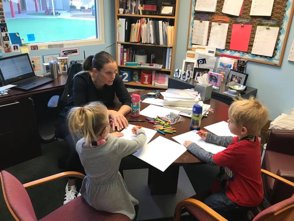 Person at desk with two children drawing