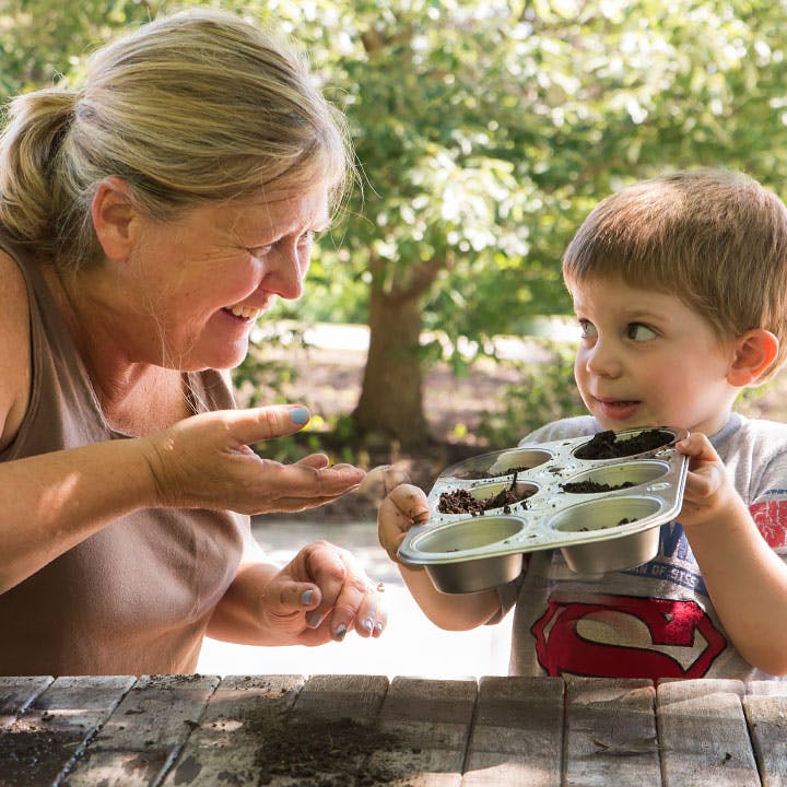 Adult and child playing with dirt in a muffin tin