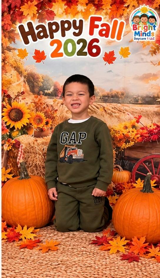 Child kneeling between two pumpkins in front of a fall themed backdrop