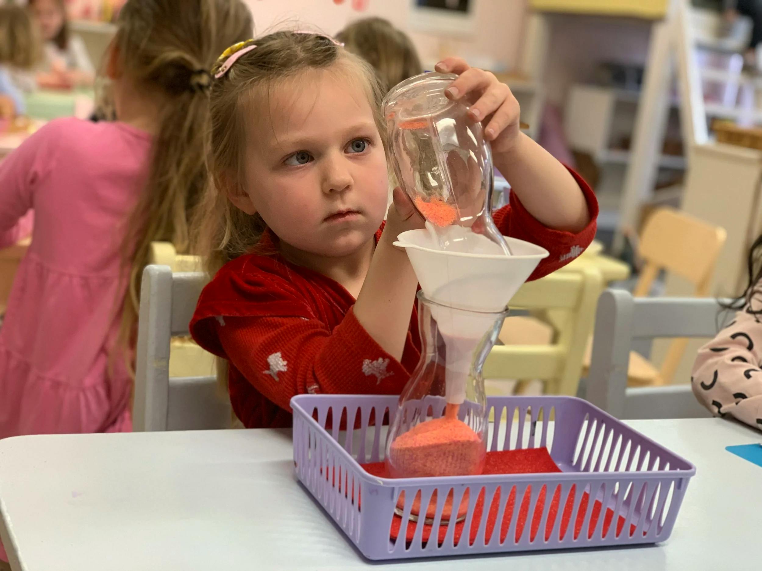 Child pouring orange sand into a funnel and hourglass