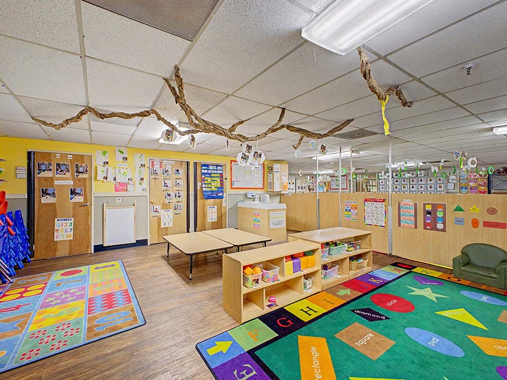 Colorful preschool classroom with tables, chairs, and play areas
