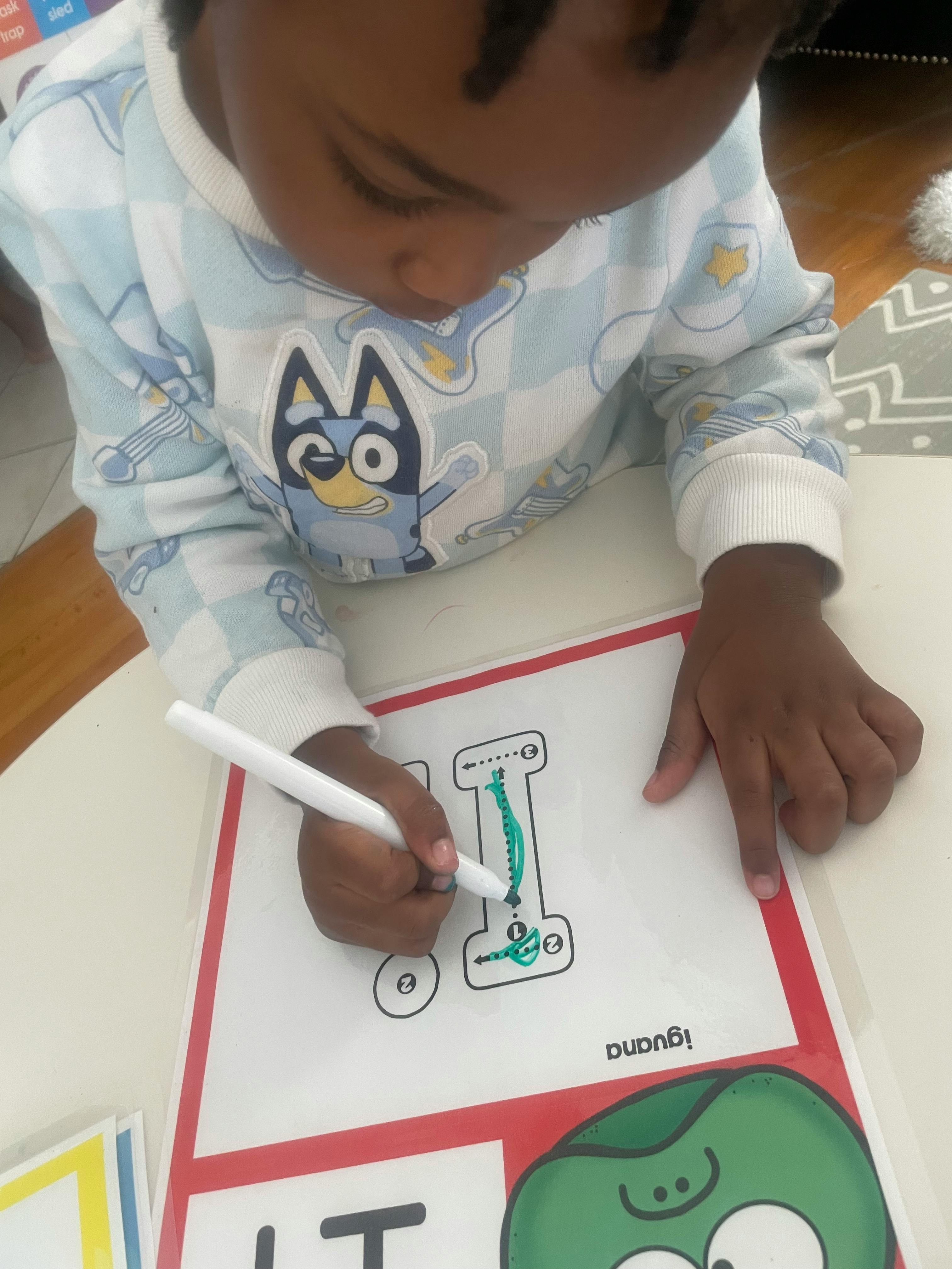 Child tracing the letter I on a worksheet with a marker
