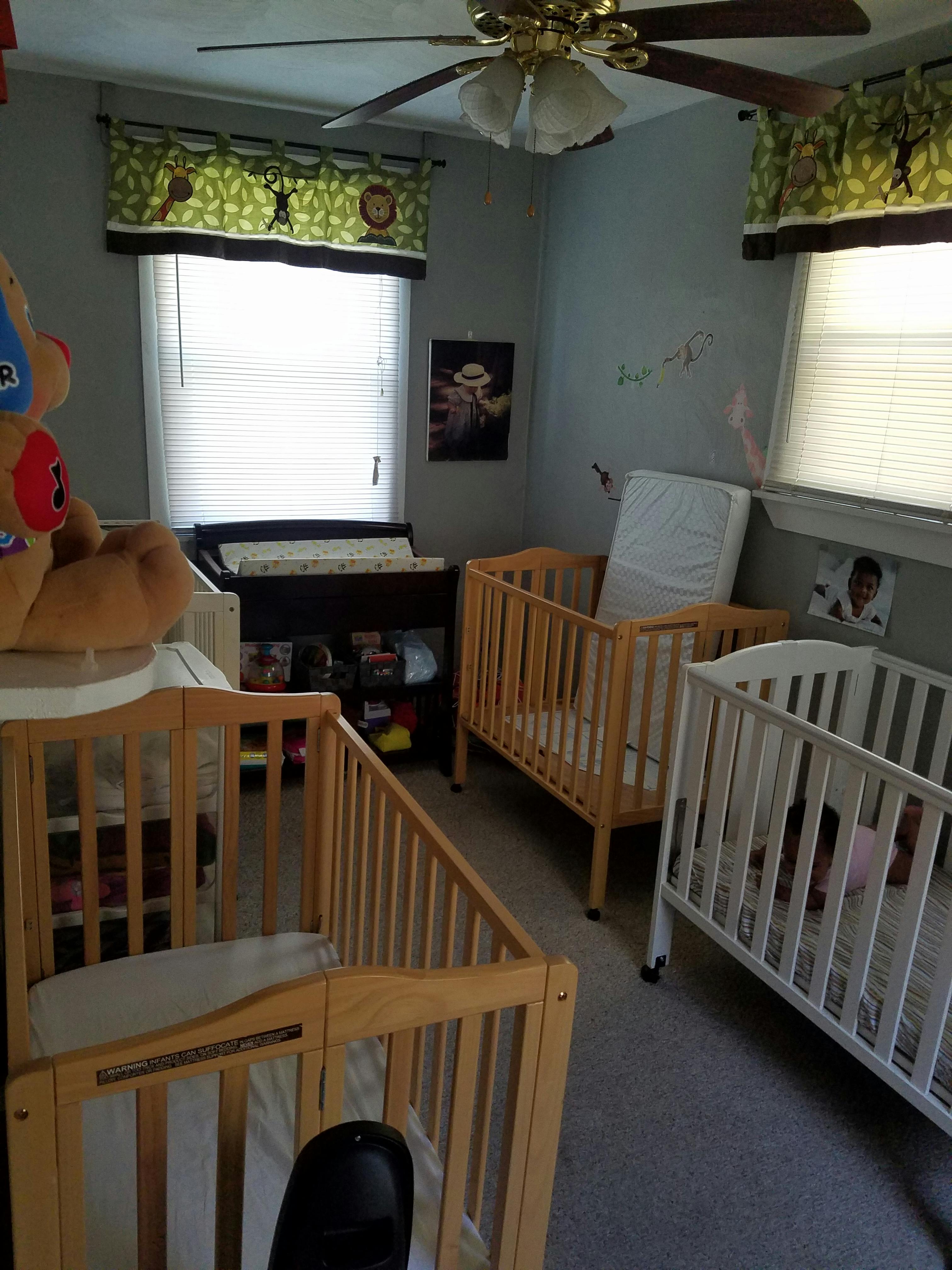 Three cribs in a room with a changing table and ceiling fan