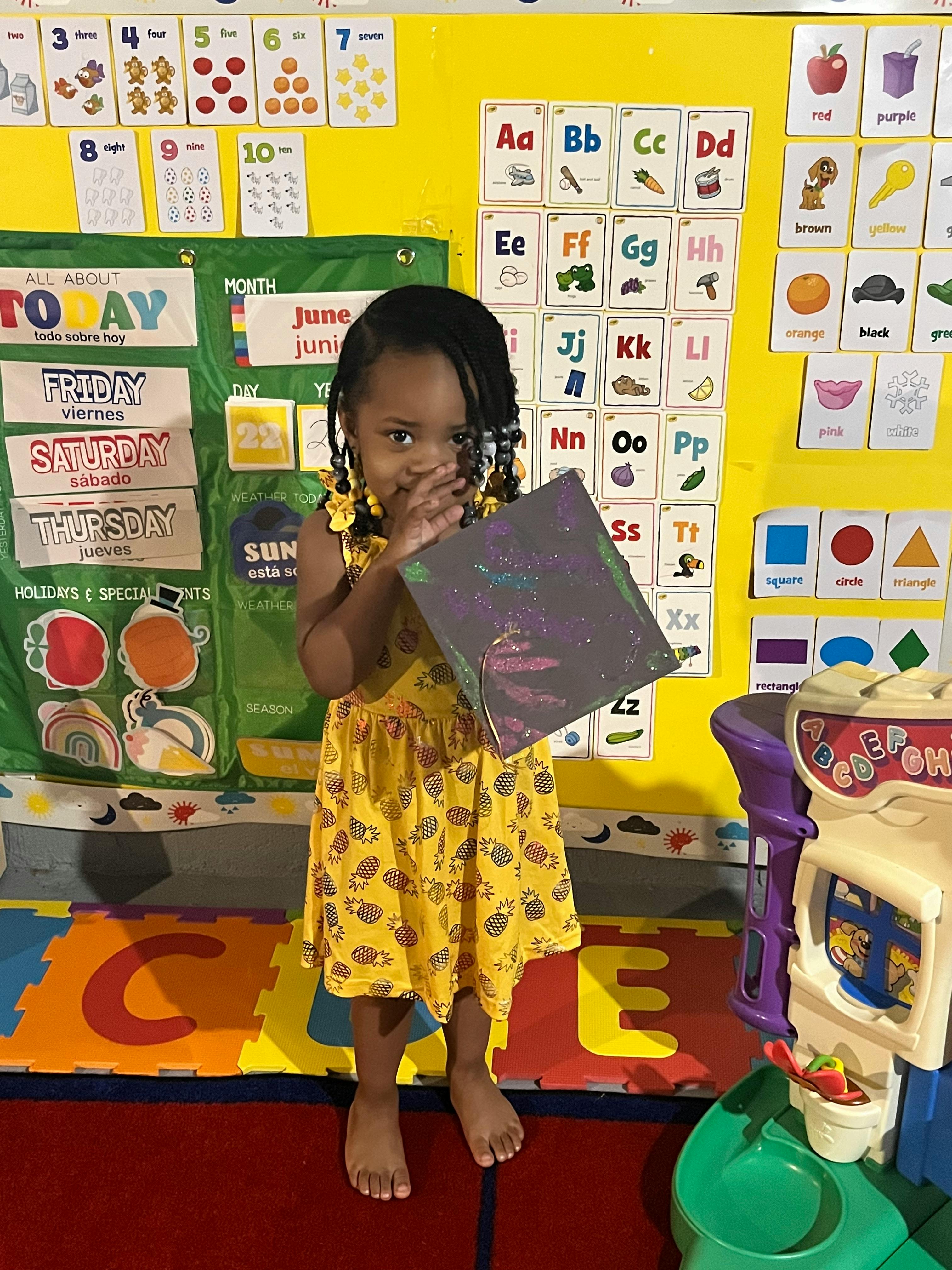 Child in a classroom holding a book in front of their face