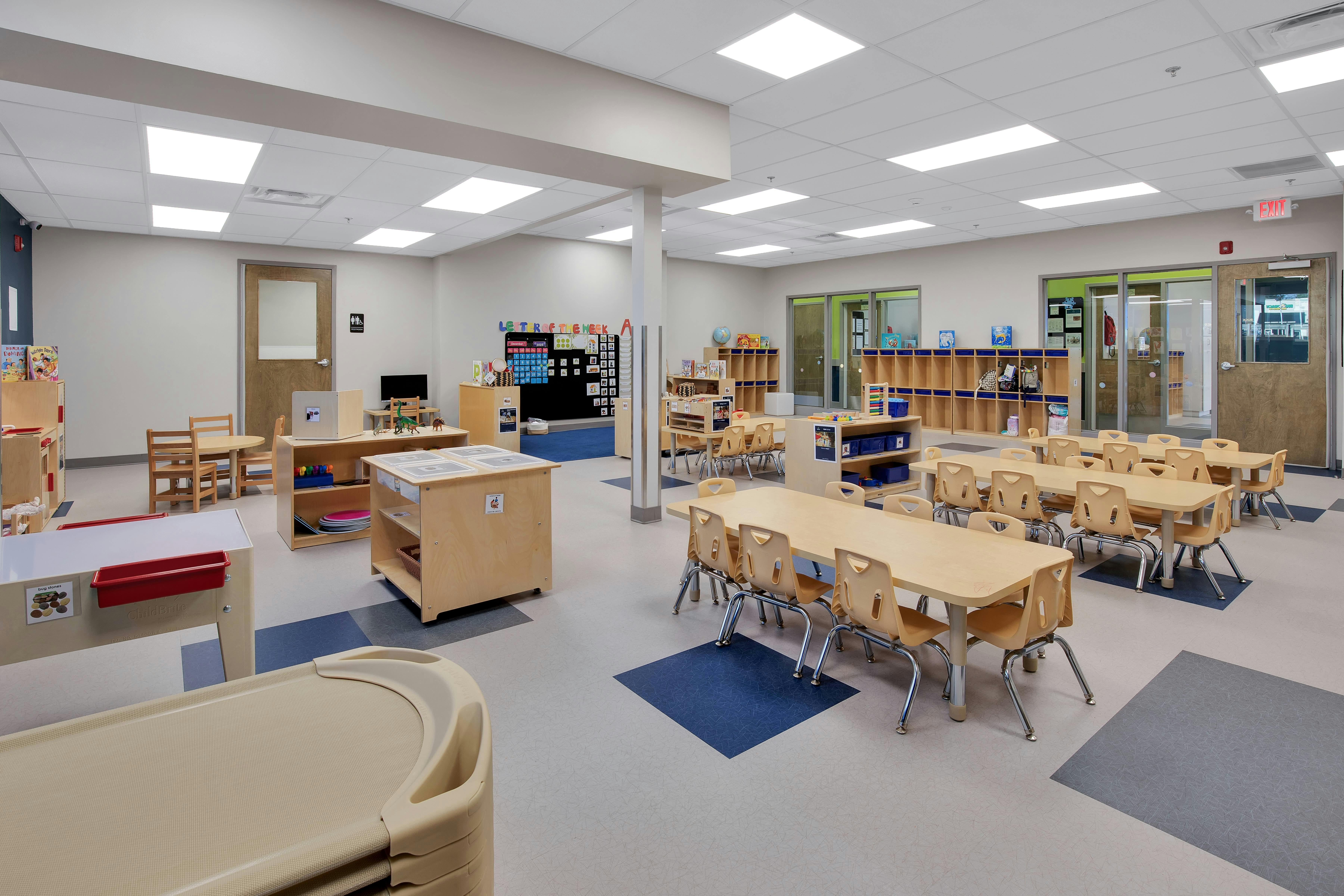 An empty children's classroom with several tables, chairs, and play areas