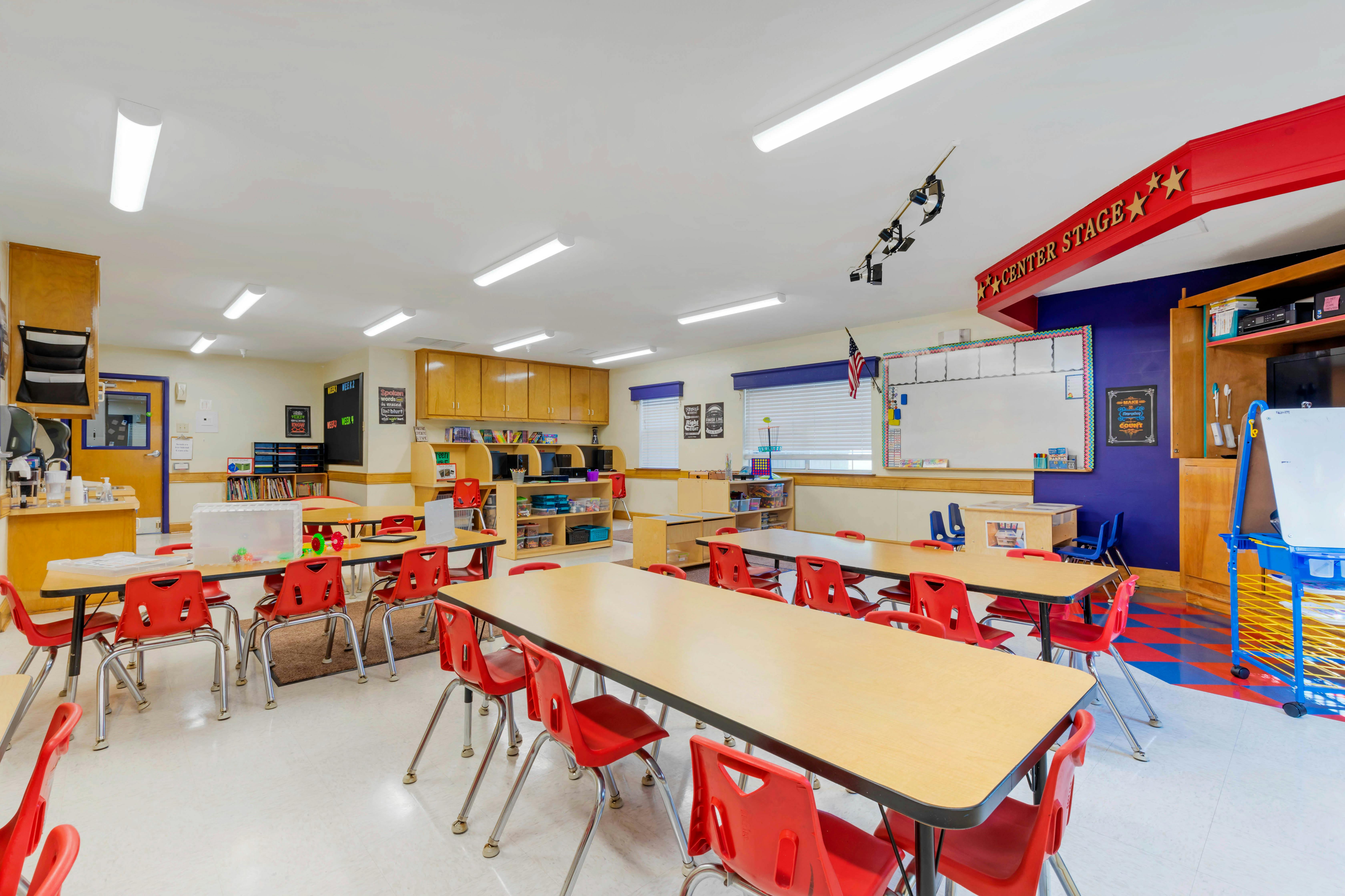 Classroom with rows of tables and red chairs, whiteboard, and learning stations