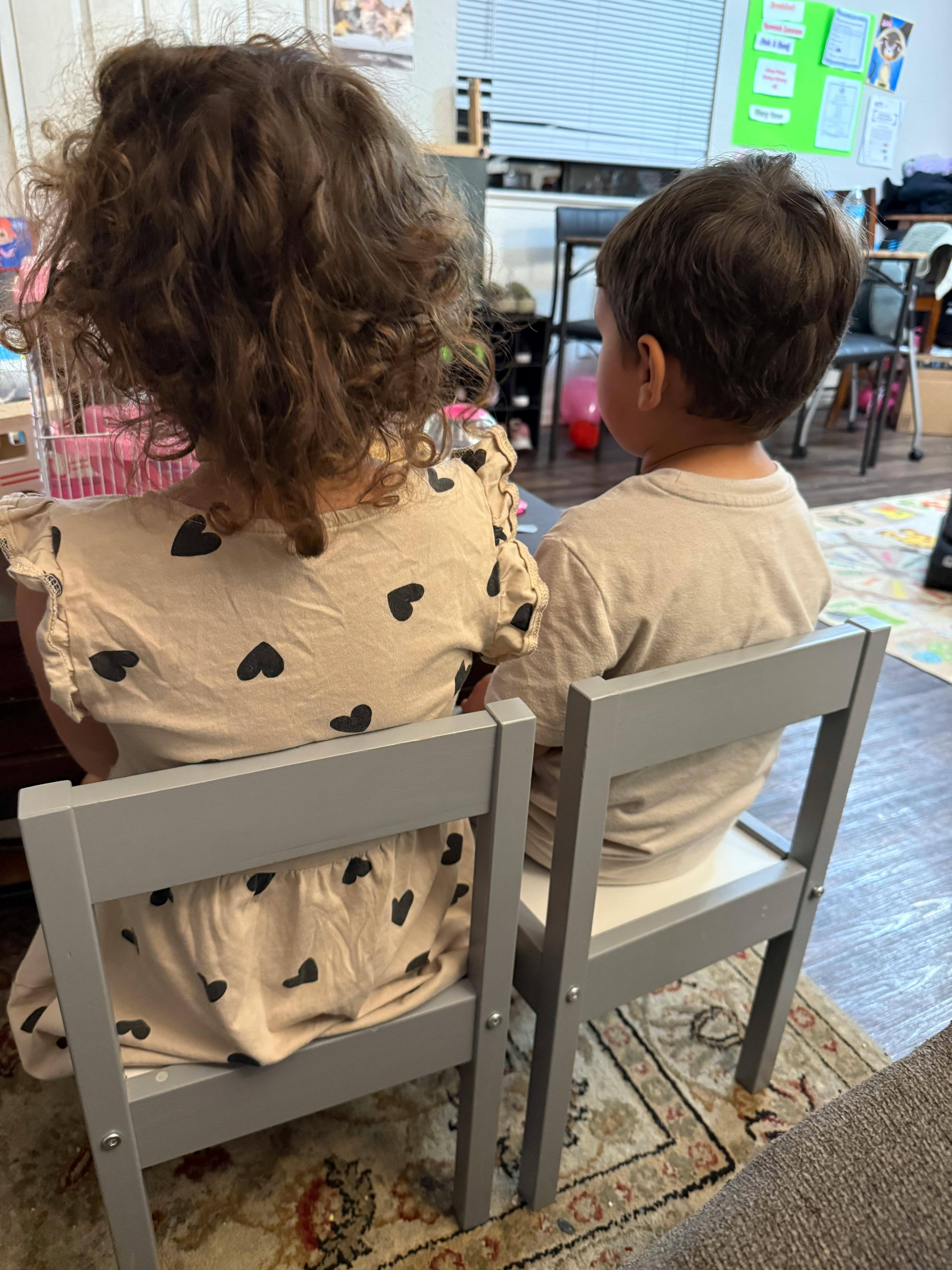 Two children sitting in chairs with their backs to the viewer