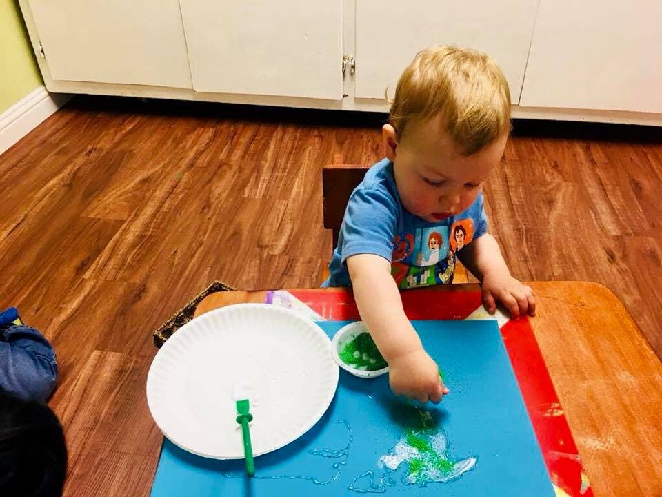 Child finger painting on blue paper at a table