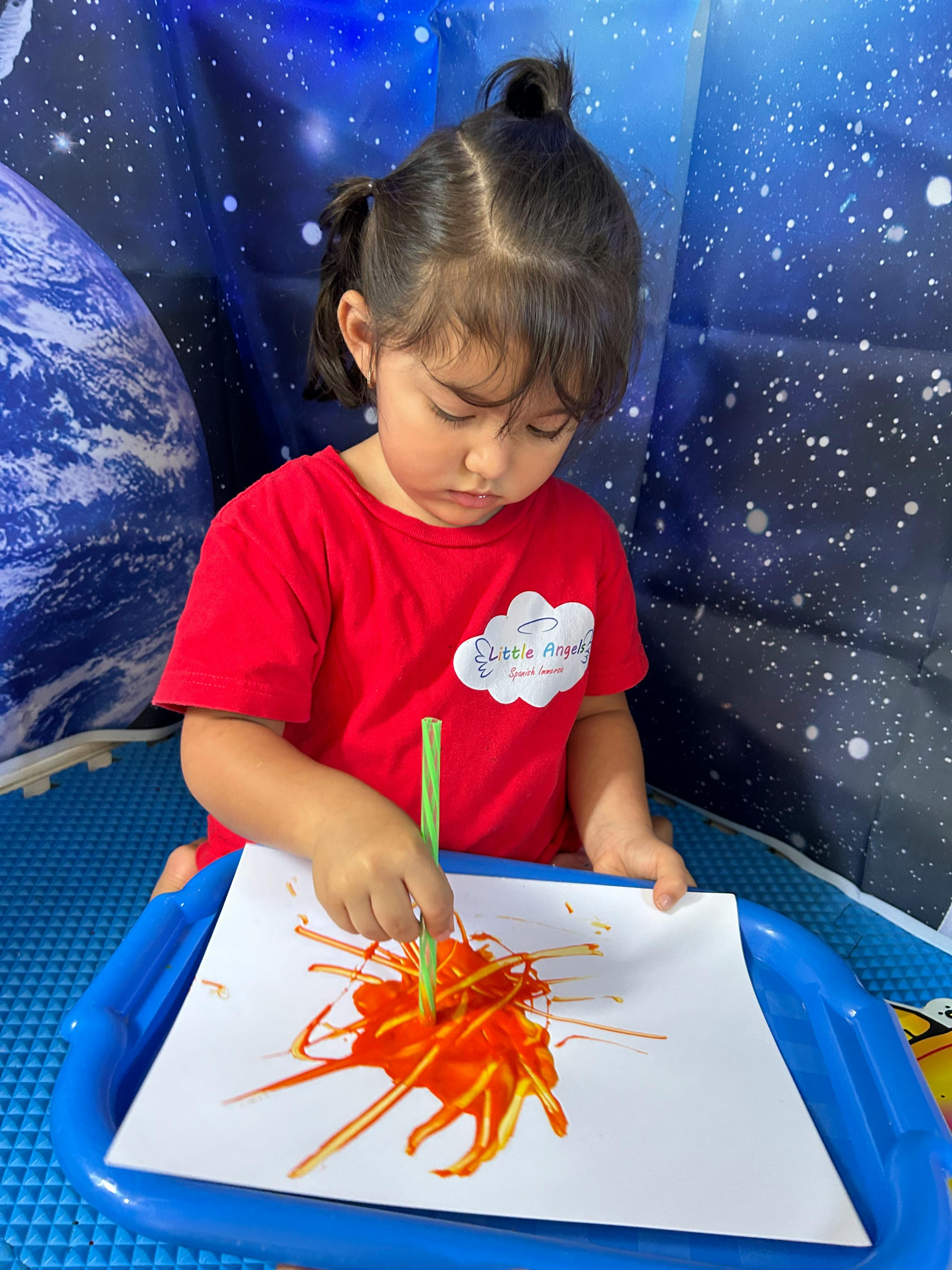 Child painting with a straw on paper