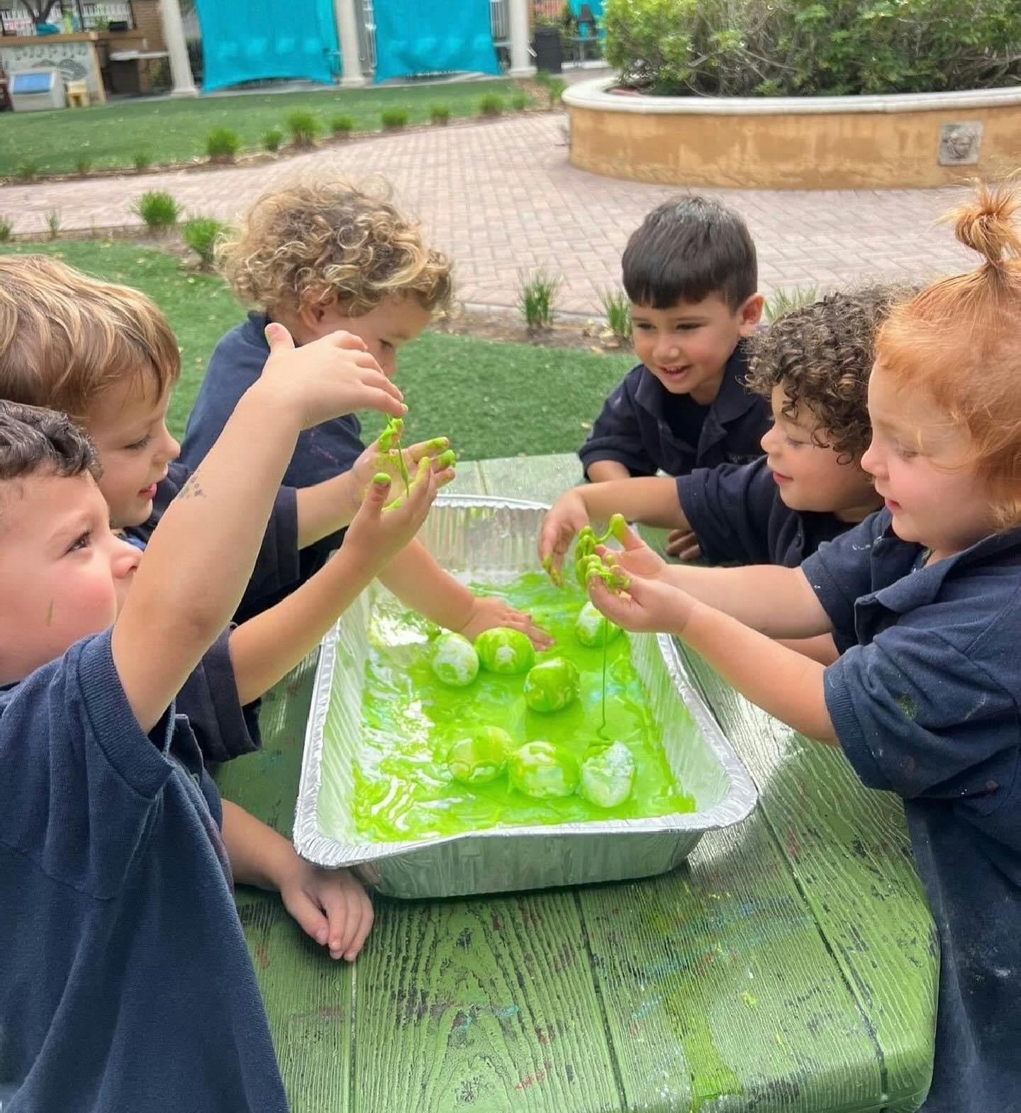 Children playing with green slime and objects in a tray