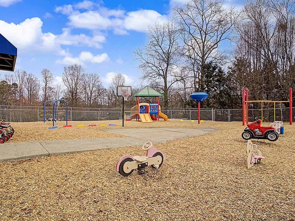 An outdoor playground with swings, slide, basketball hoop, and spring riders