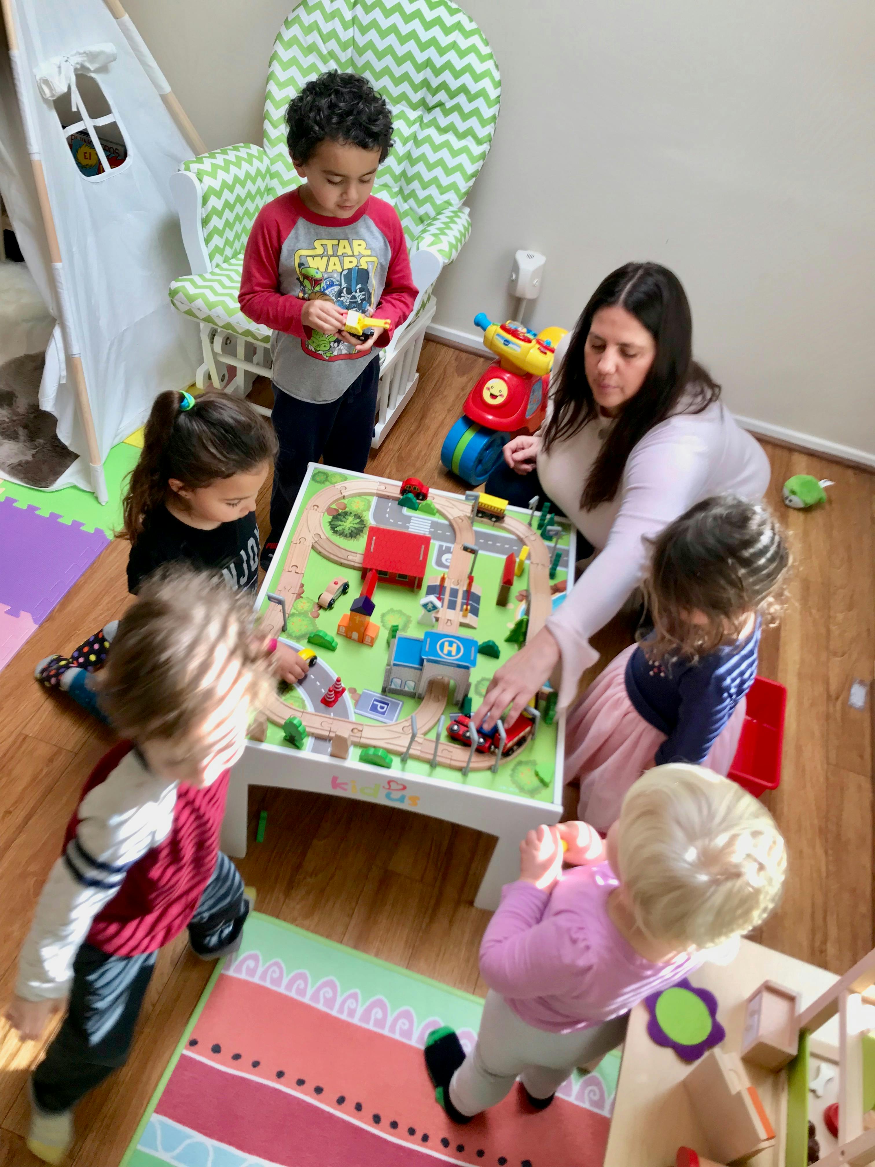 Adult and multiple children playing with a toy train set on a table