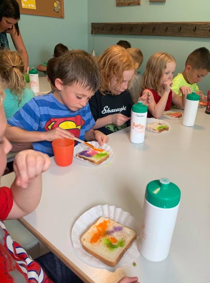 Children painting on slices of bread at a table