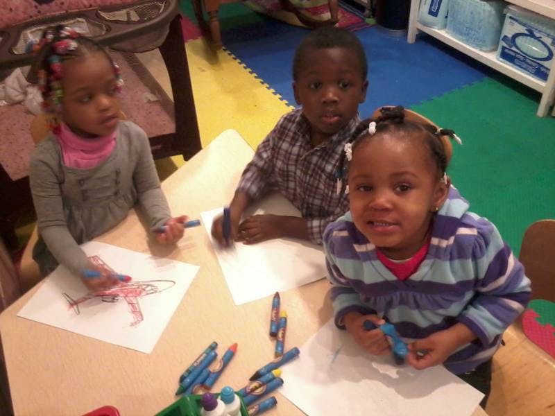 Three children drawing with crayons at a table