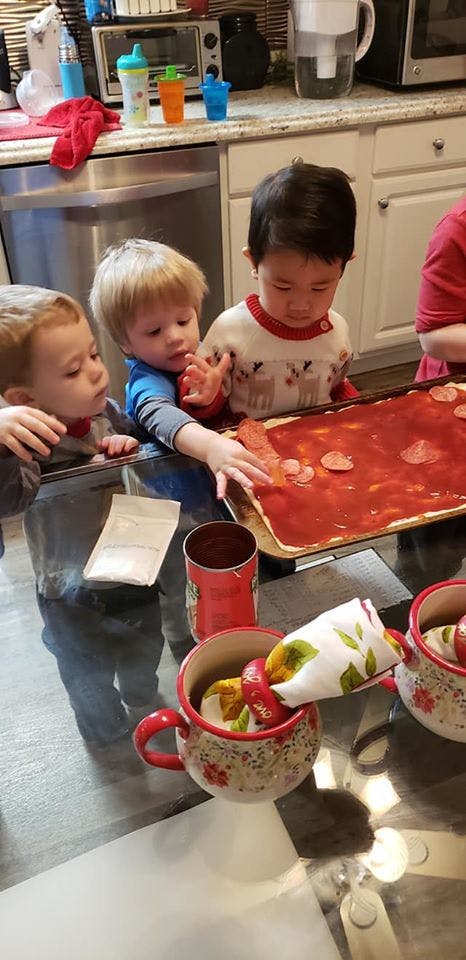 Three children making pizza in a kitchen