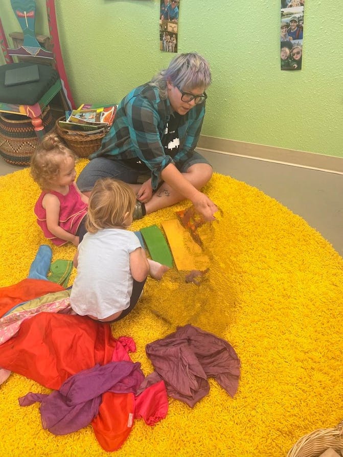 Person and two children playing on a yellow rug