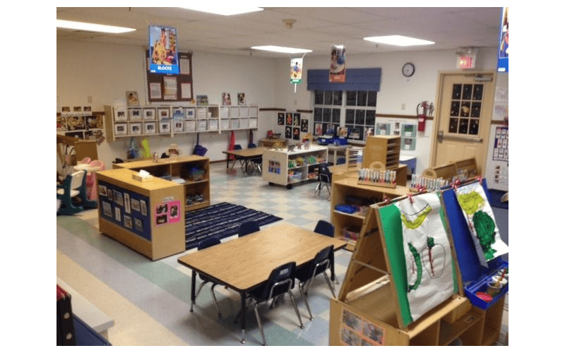 Empty classroom with small tables and chairs, shelves, and art easels