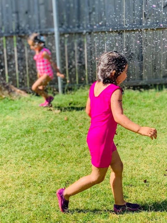 Two children playing in a sprinkler on a grassy lawn