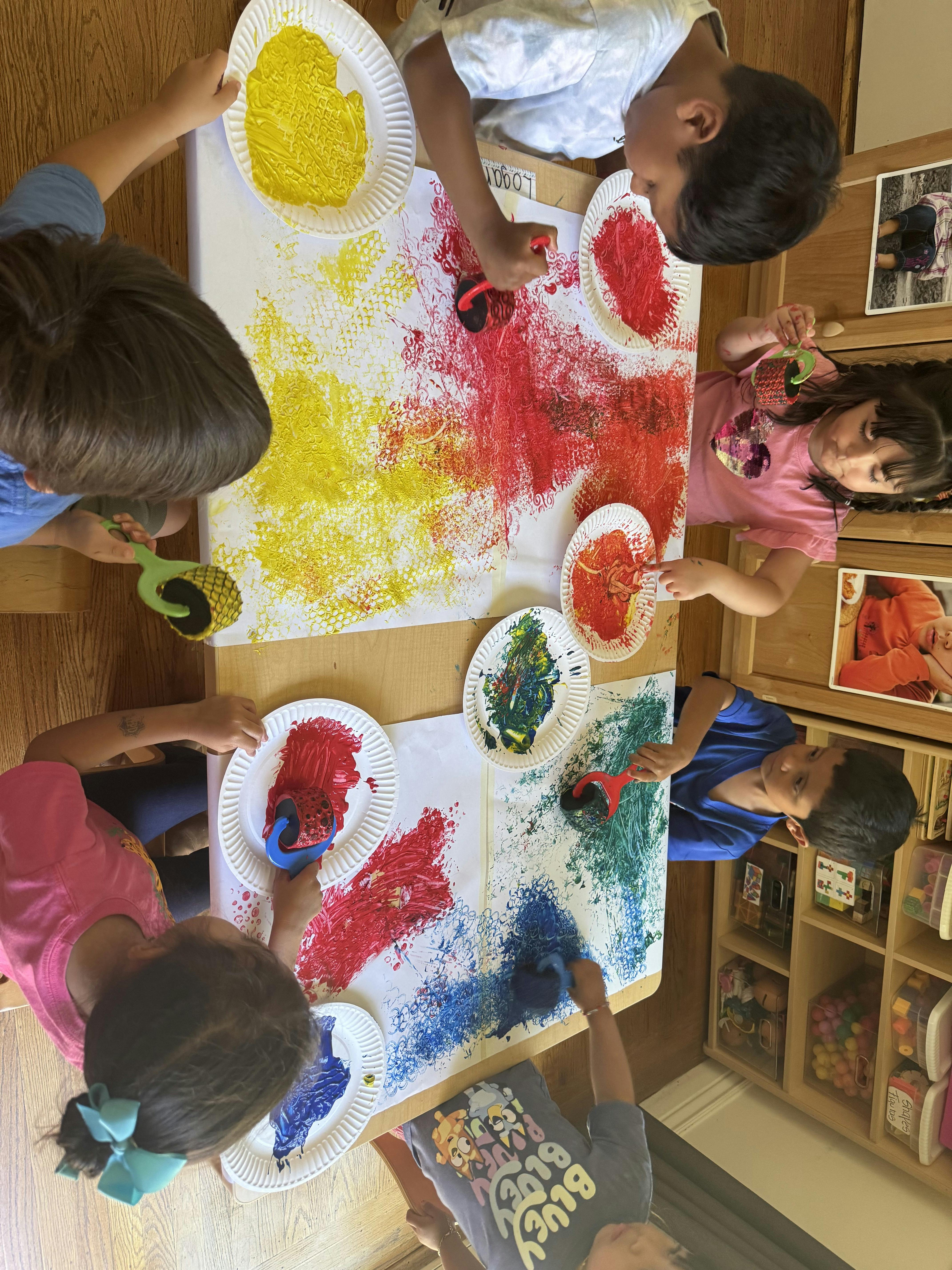 Children painting with rollers and colorful paint on a large sheet of paper