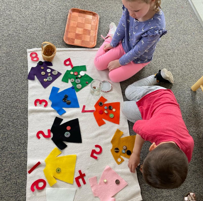 Two children playing with felt shirts and buttons on a mat