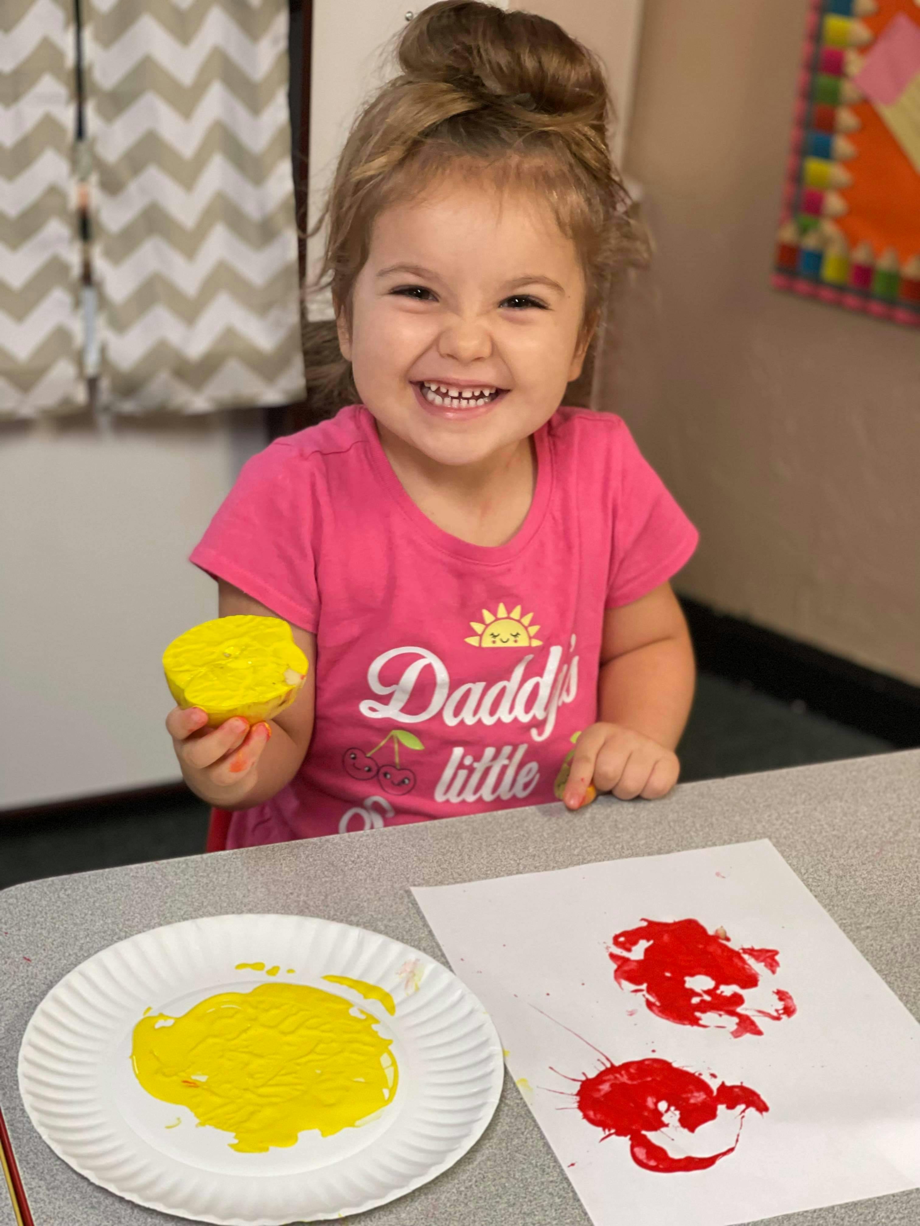 Child holding a yellow sponge, with paint on a paper plate and paper