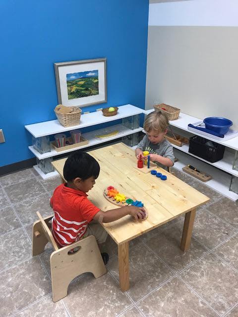 Two children playing with colorful blocks at a wooden table in a classroom
