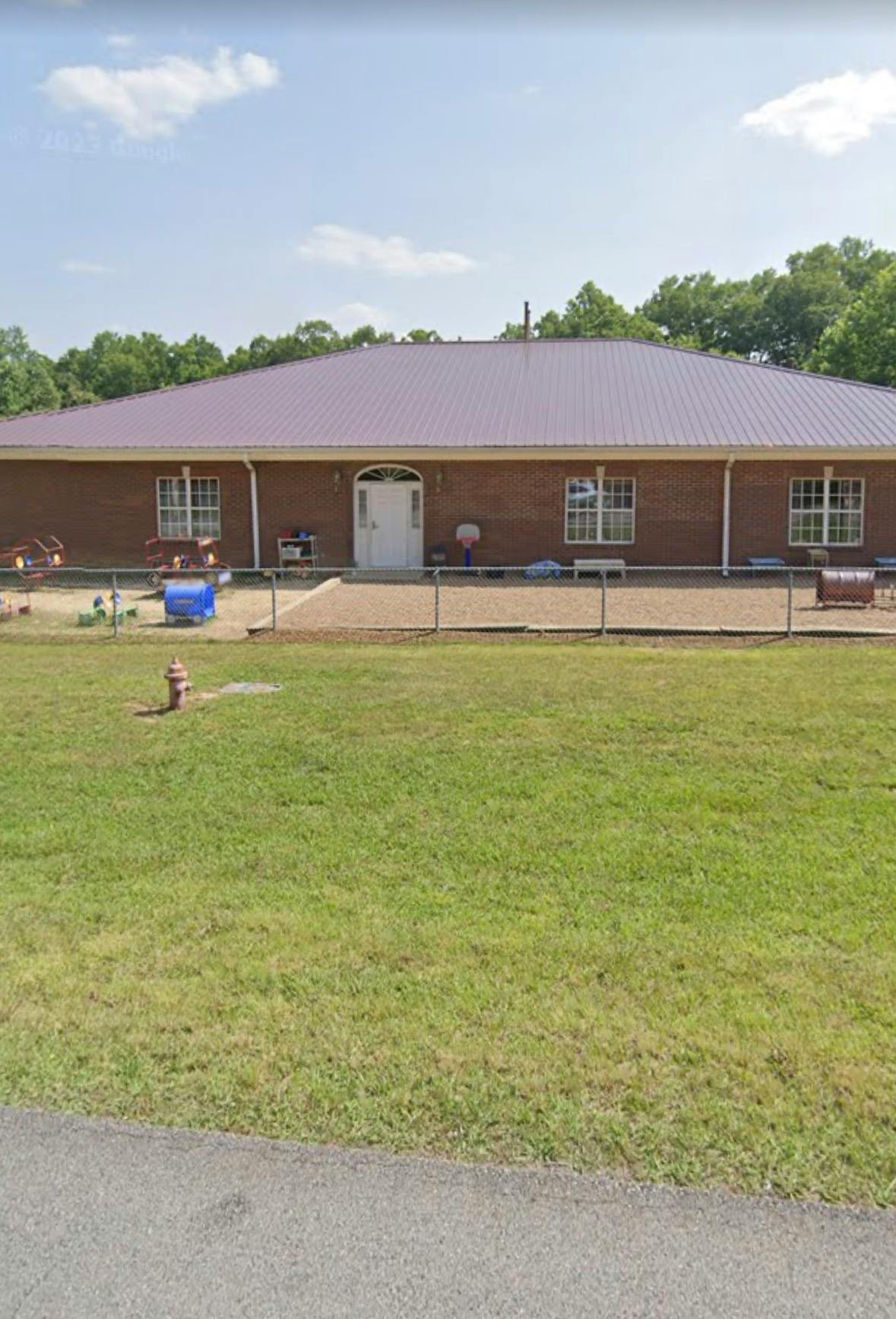 Brick building with a metal roof and a fenced playground area