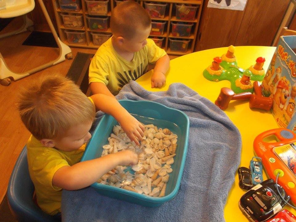 Two children playing with items in a blue bin on a yellow table