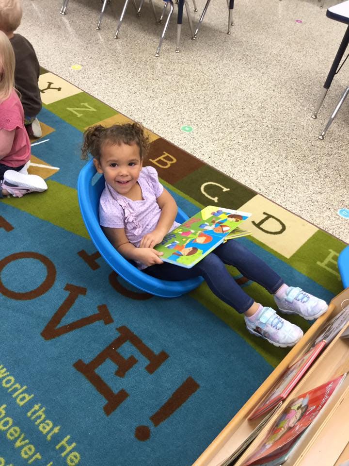 Child sitting in a blue chair holding a book on a rug