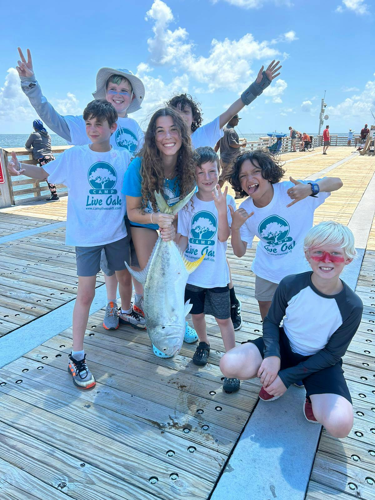 Group of people and children on a pier holding a large fish