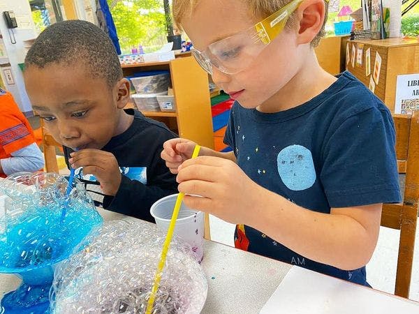 Two children blowing bubbles with straws in a classroom